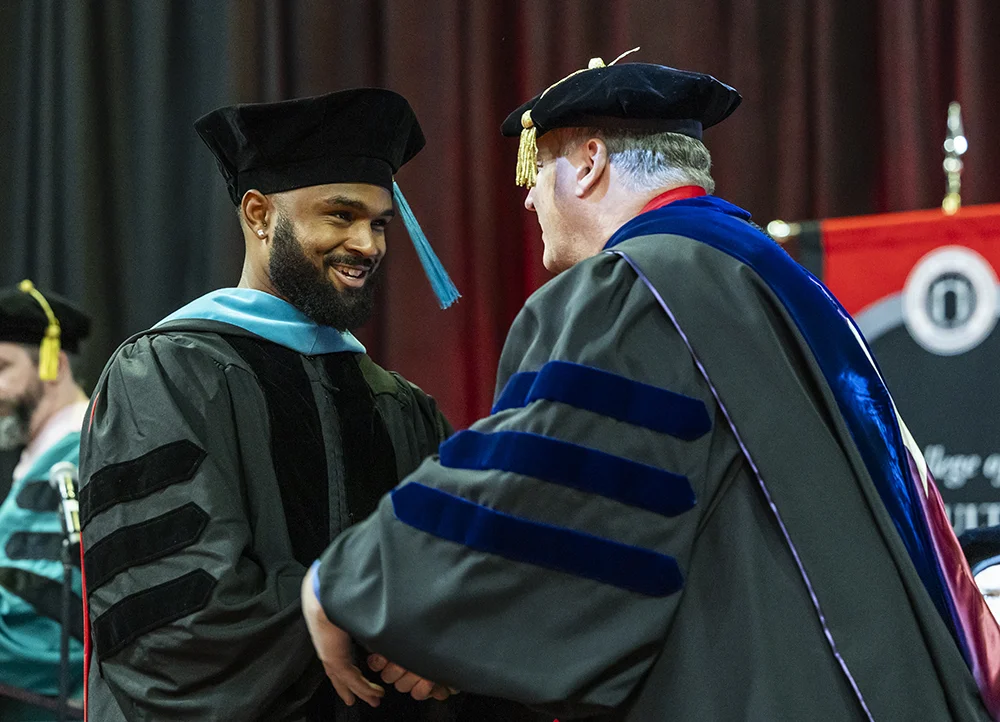 A-State graduate smiles and shake hands with his dean while accepting diploma.