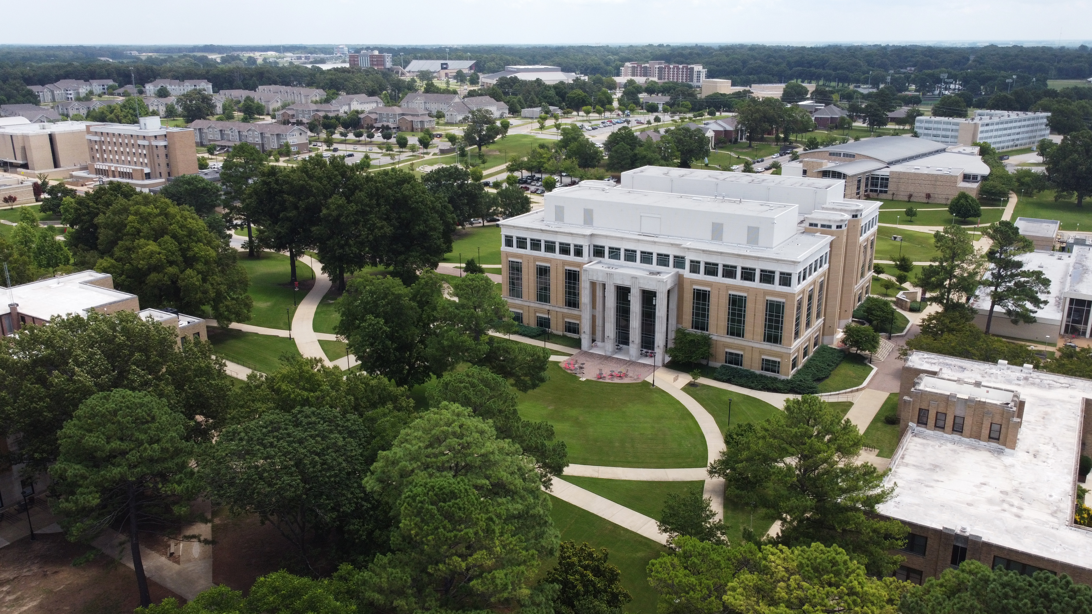 Aerial view of A-State campus in summer, featuring the Humanities and Social Sciences Building surrounded by trees, sidewalks, and nearby academic buildings.