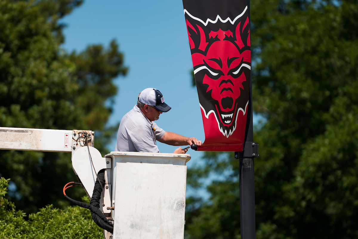 A worker installs a red wolf banner on a light pole.