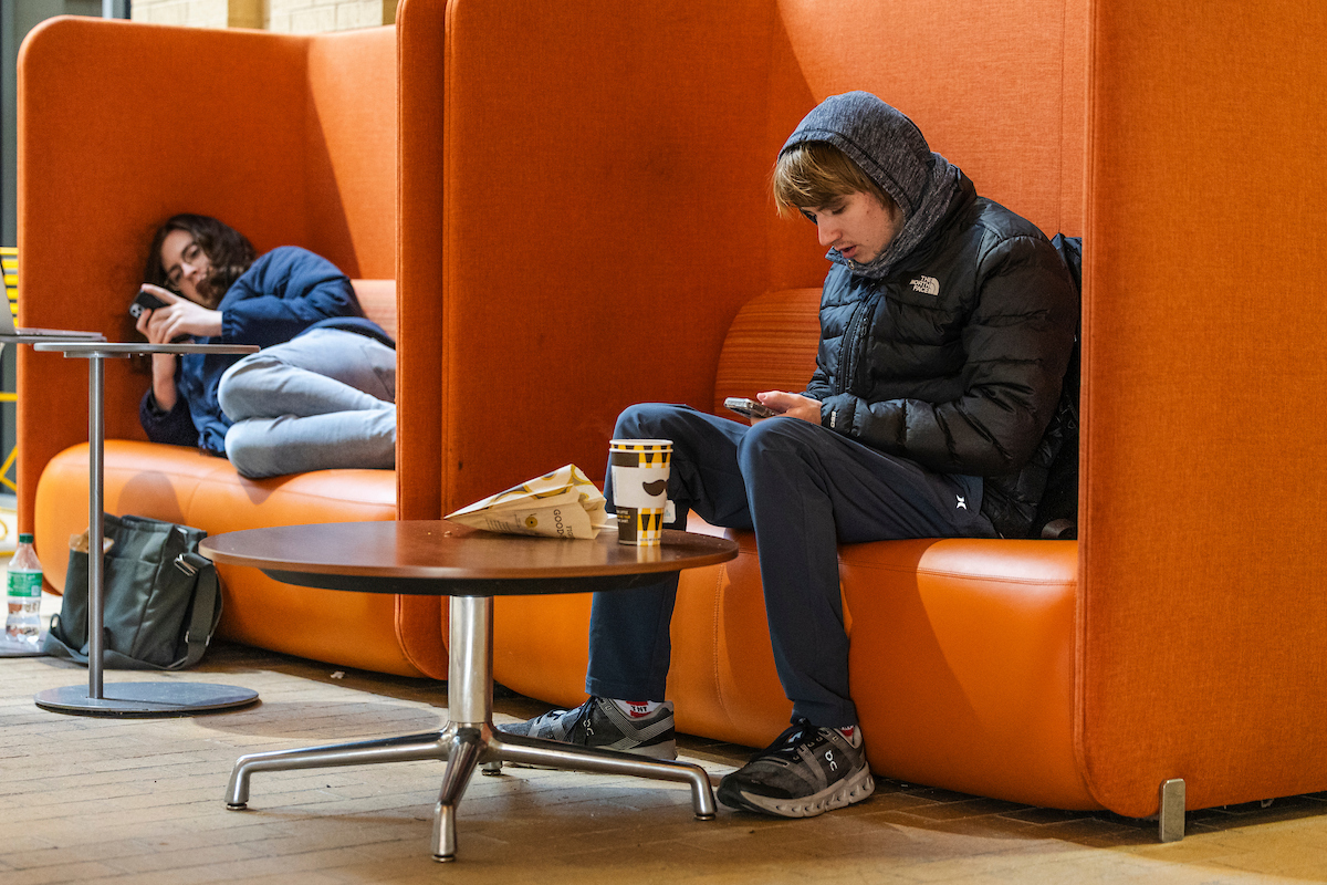 Students look at their phones while waiting to change classes in the Humanities building.