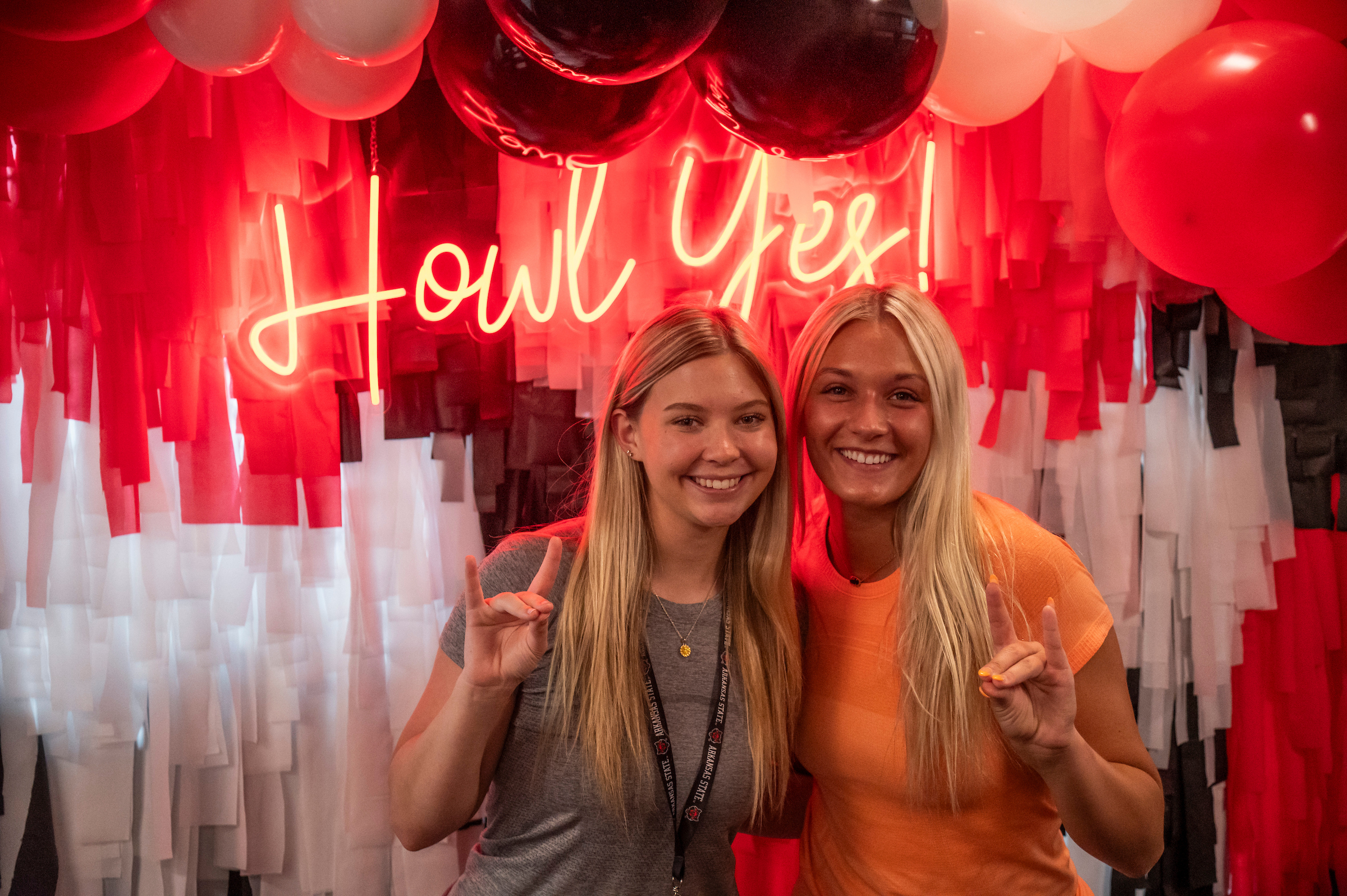 Two smiling students pose in front of a red and white “Howl Yes!” backdrop with balloons.