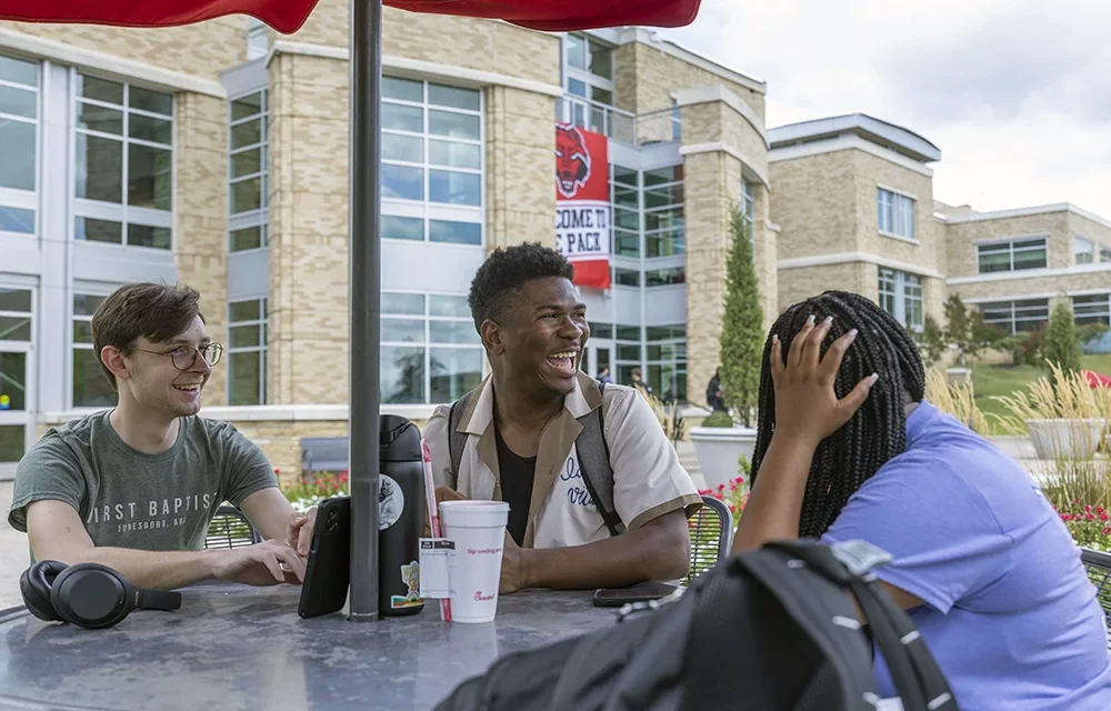 Three students laughing together at a table.