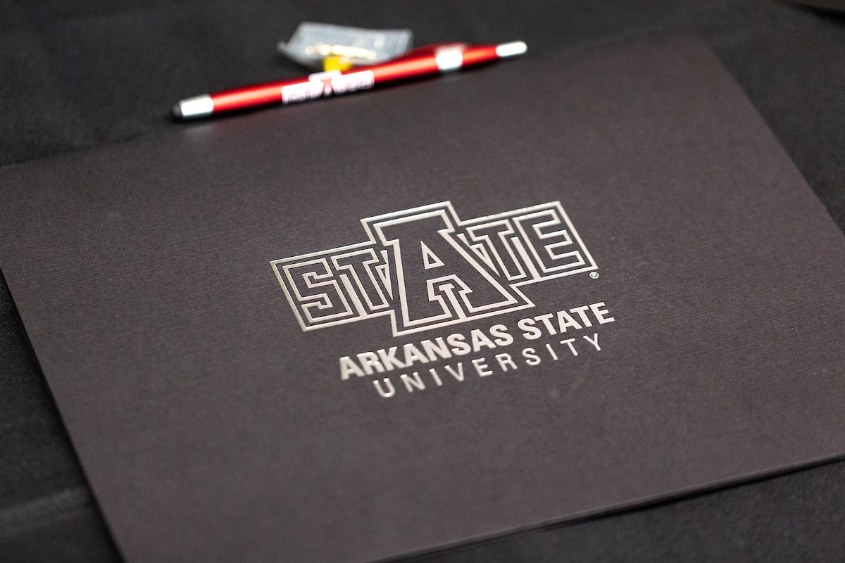 Close-up of Arkansas State University folder with logo and pen on black tablecloth.