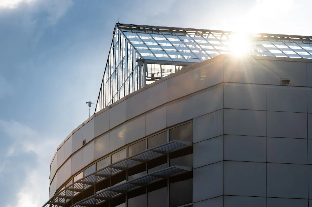 Sunlight shining through glass panels of a rooftop greenhouse on a modern campus building.