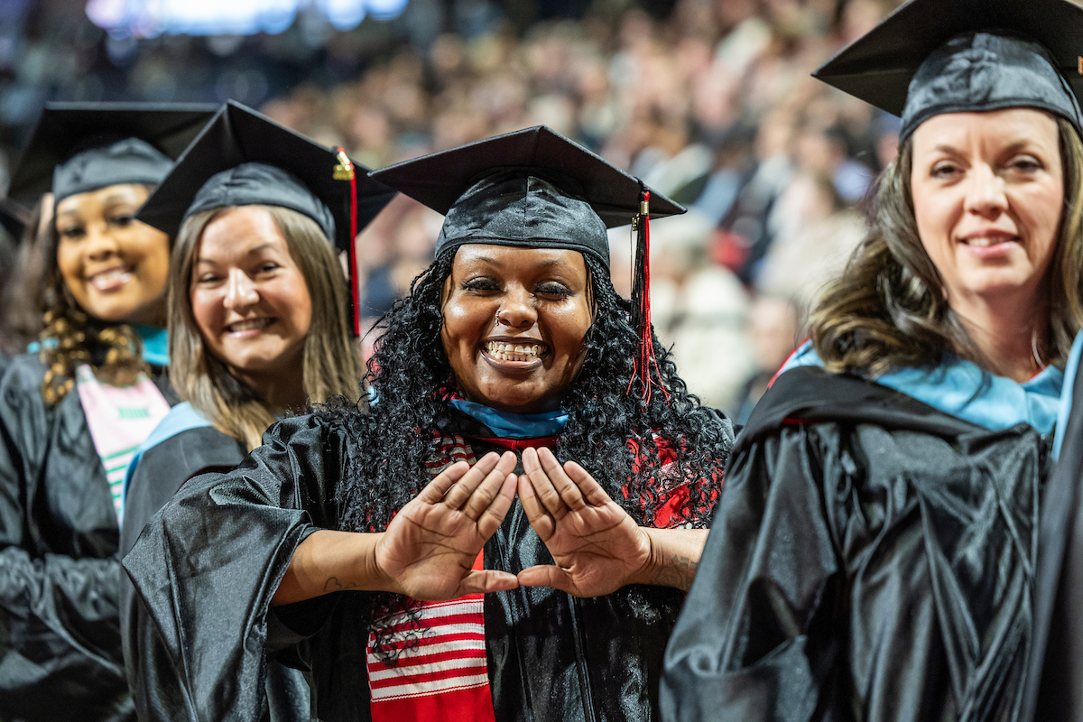 A-State graduates smile and celebrate in caps and gowns during commencement ceremony.