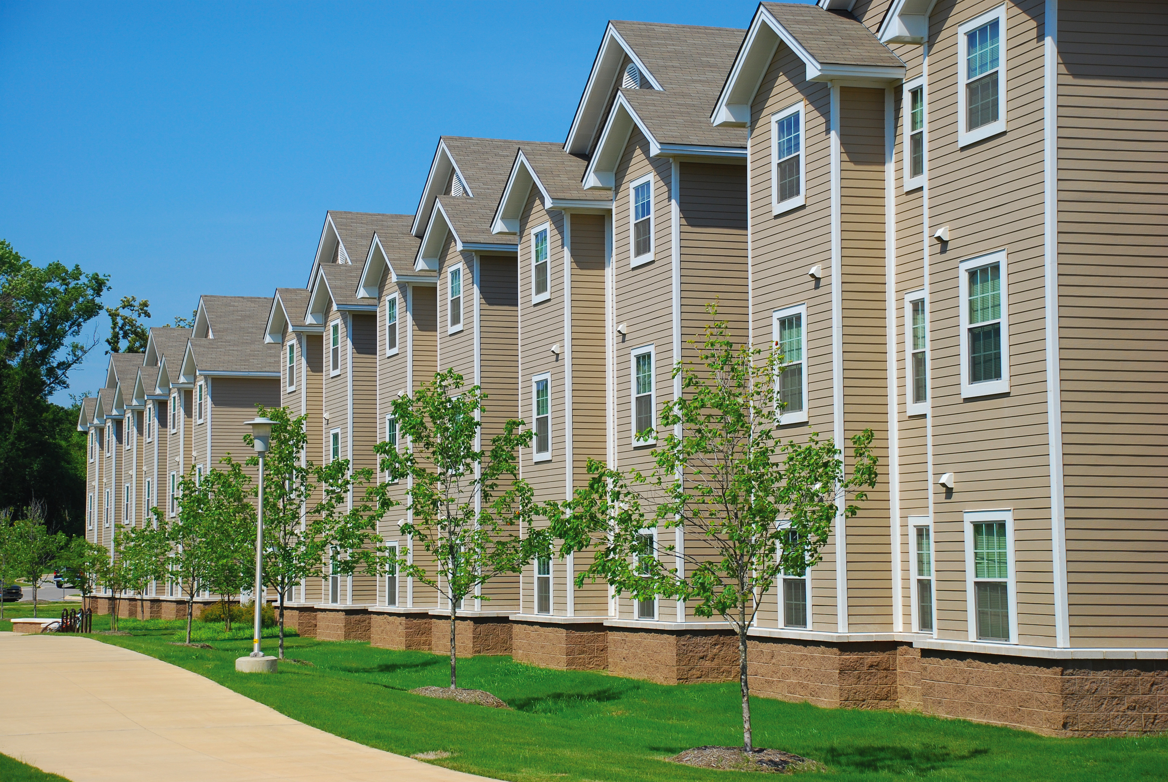 Row of modern student apartment buildings with trees and bright green lawn at A-State.