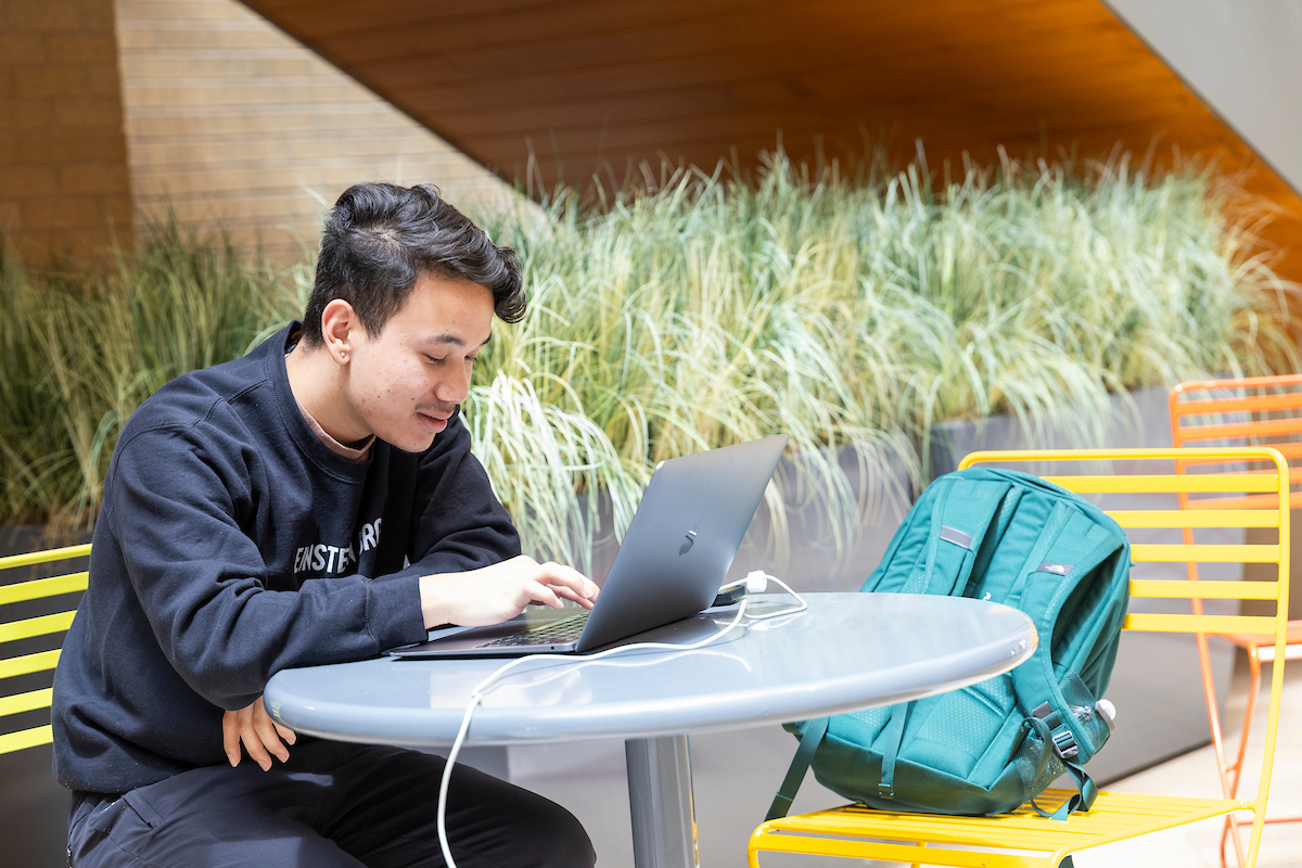 A-State student works on laptop at a round table with backpack in a bright indoor campus space.