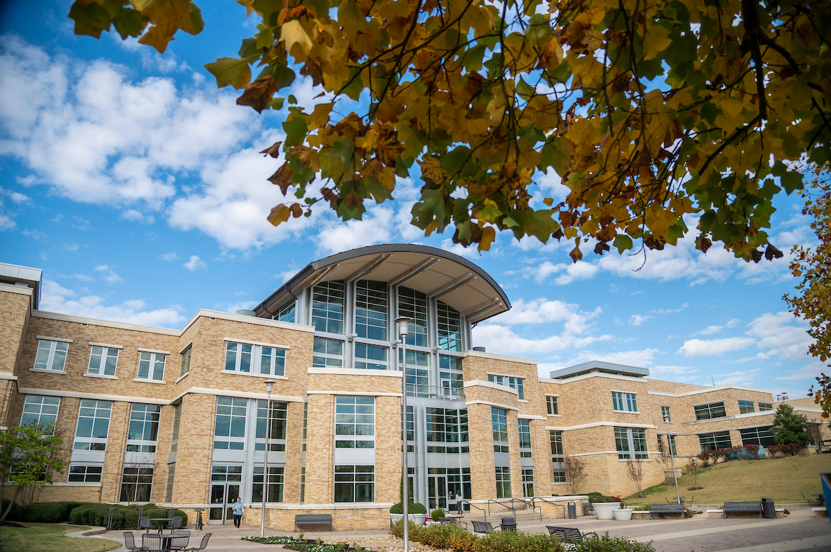 Reng Student Union framed by yellow autumn leaves under a partly cloudy blue sky.
