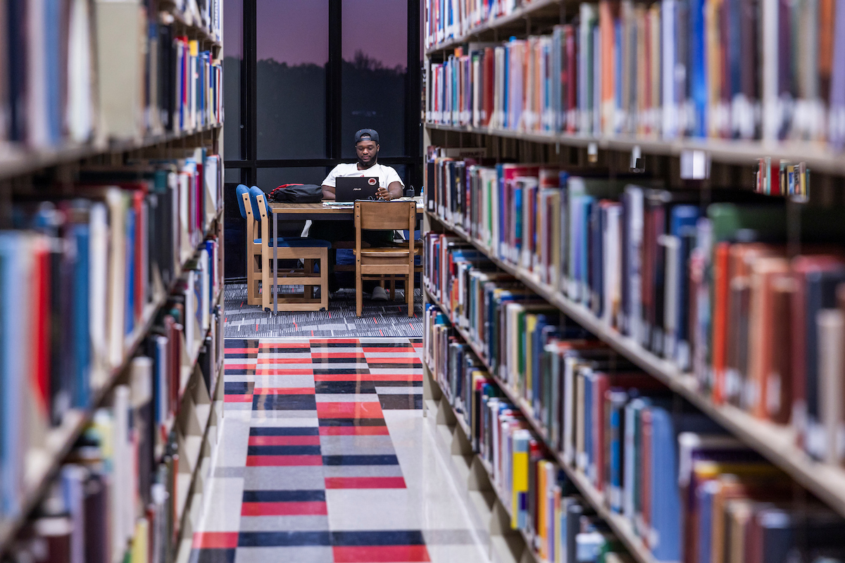 A-State student studies in the library during the evening surrounded by books.