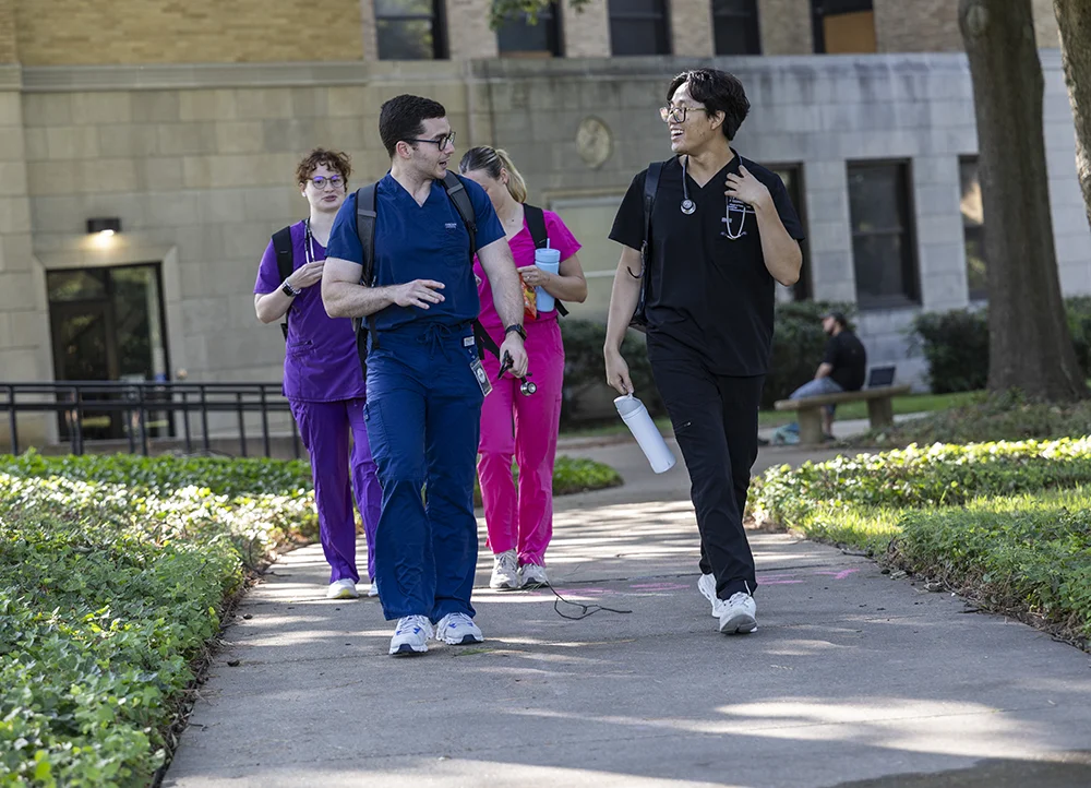 NYITCOM students in scrubs laughing on campus.