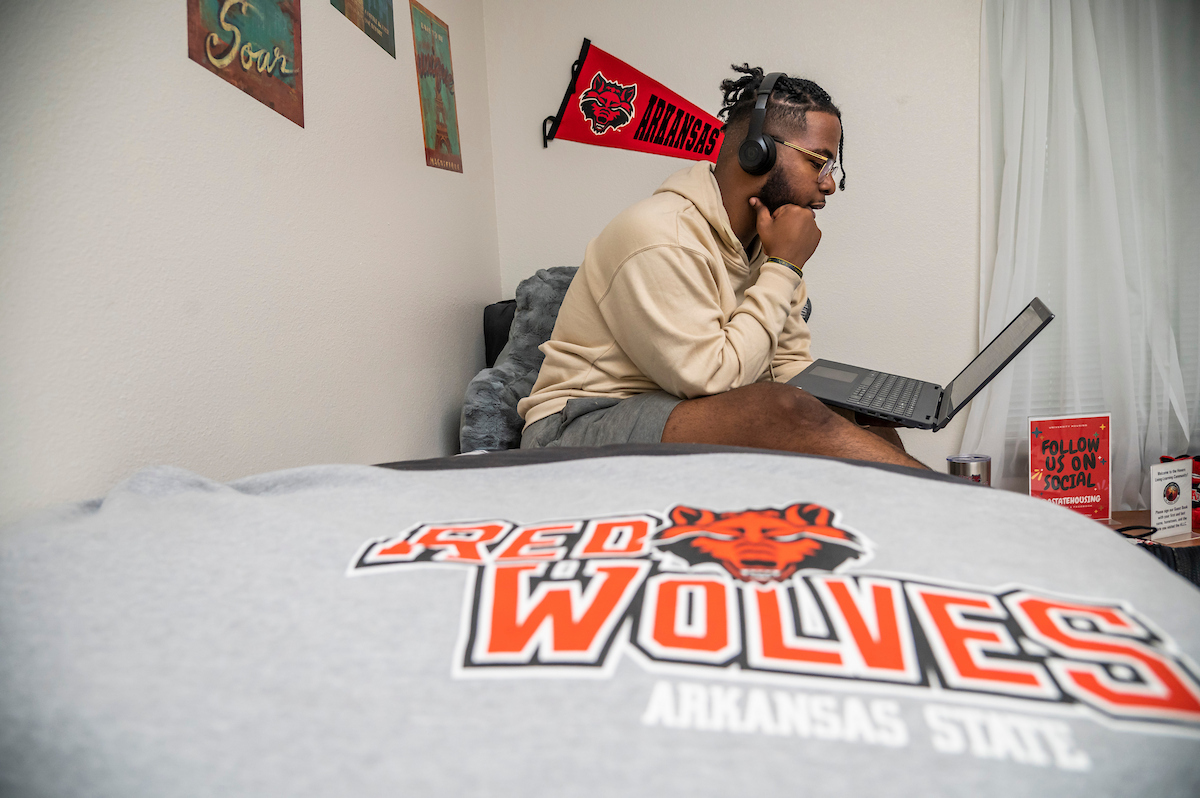 Student studying on his bed in his dorm with Red Wolves bedspread.