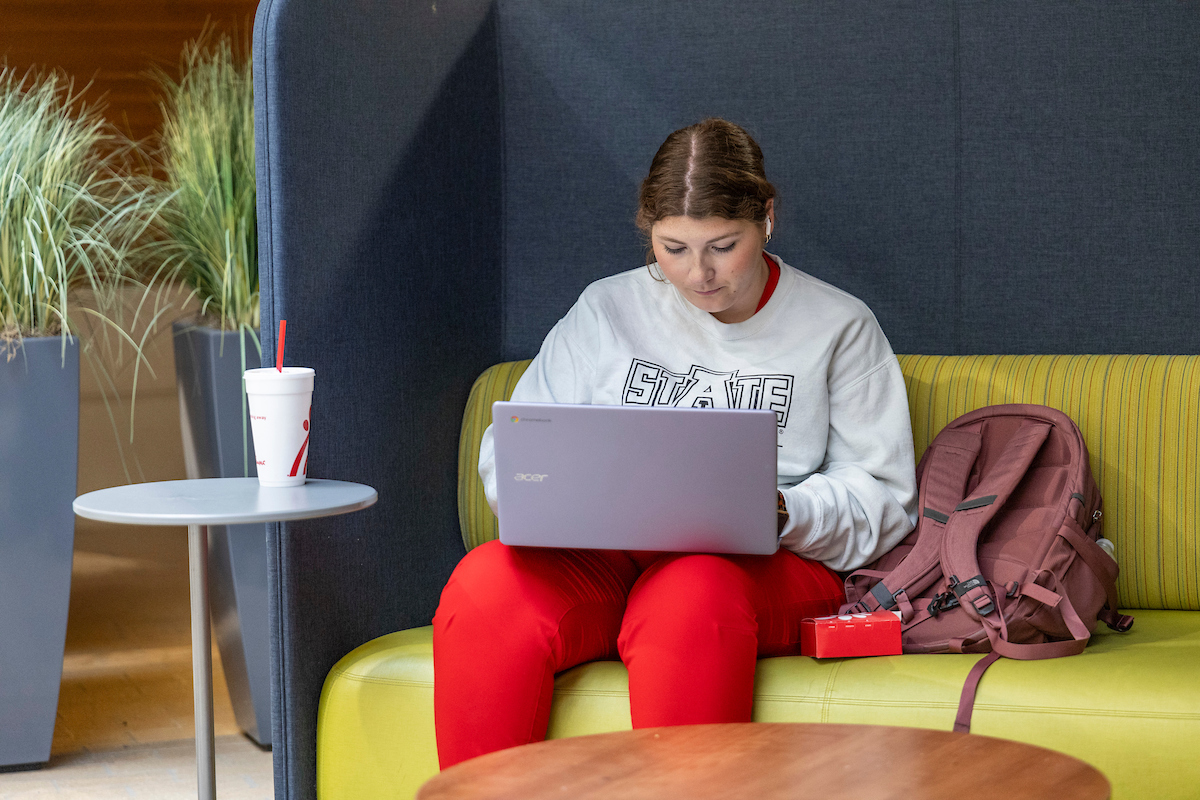 A-State student focused on laptop while studying in a comfortable lounge spot.