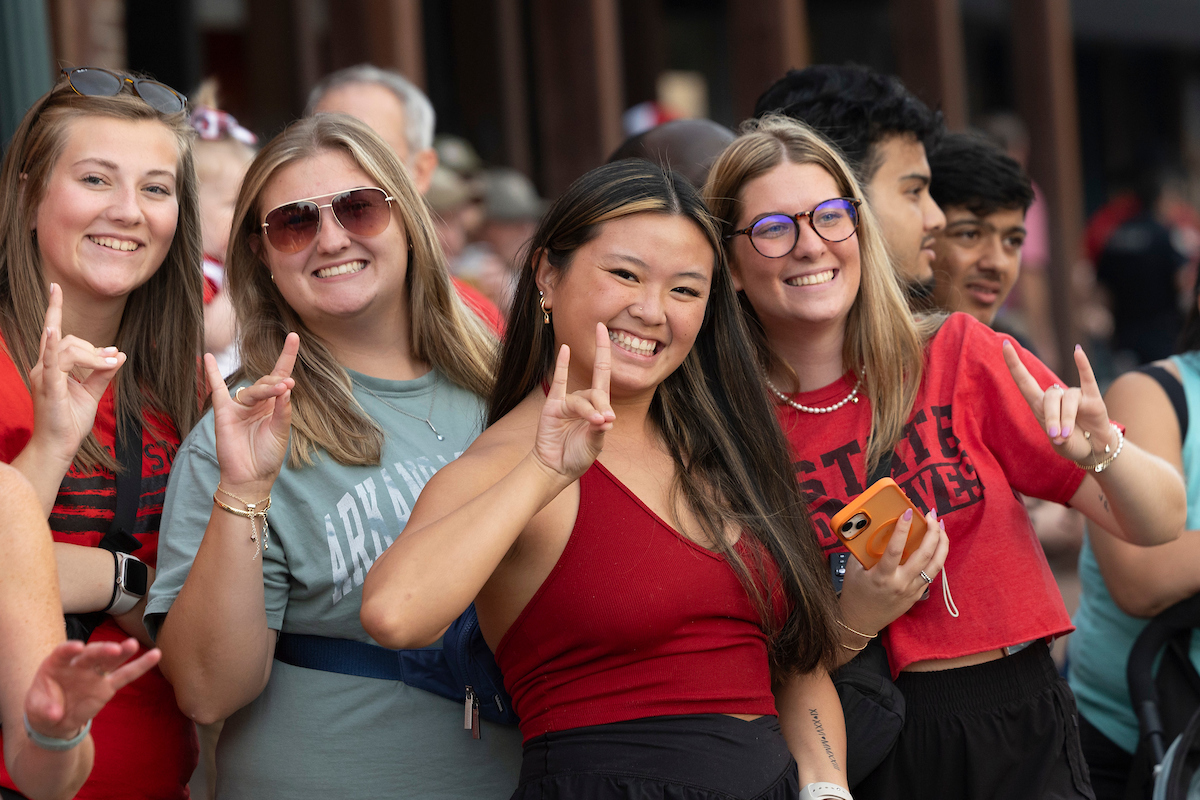 A group of four smiling students make the Wolves Up hand gesture at an A-State athletic event