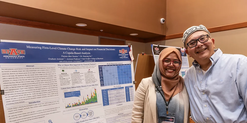 Faculty member poses with graduate student in front of research presentation.