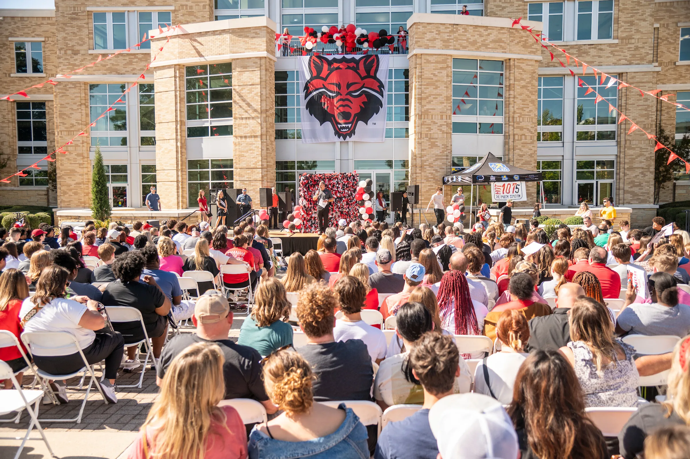 Crowd of students and guests attend an outdoor recruitment event in front of the union decorated with the Red Wolf banner.