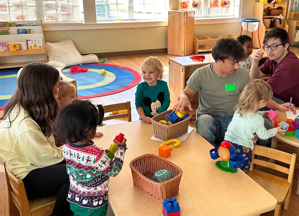 children and adults in a daycare setting with short tables and toys