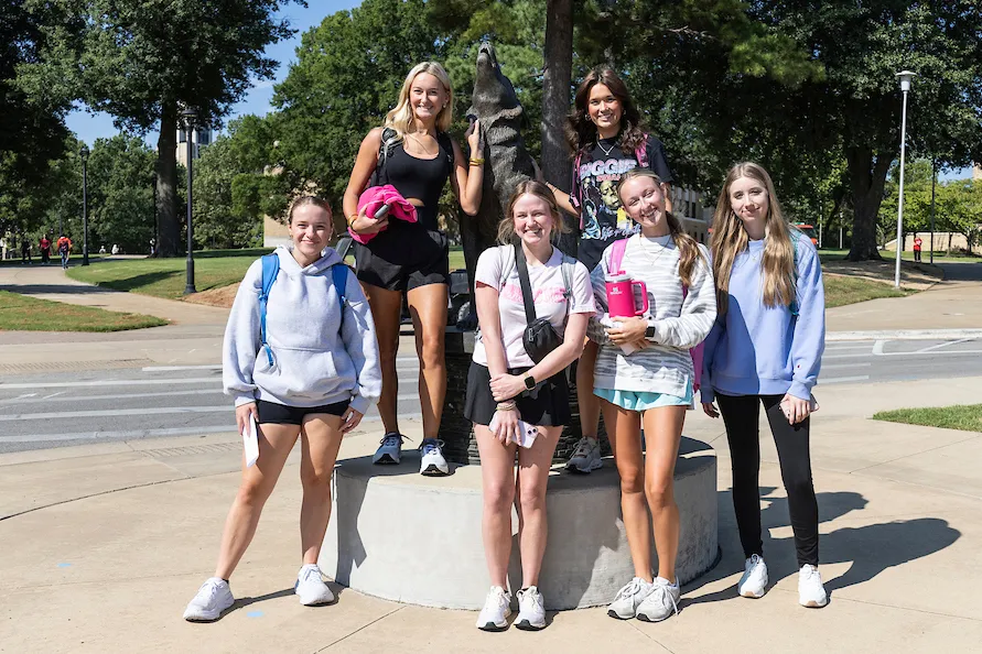 A-State students gather around the wolf statue for a group photo on a sunny day.
