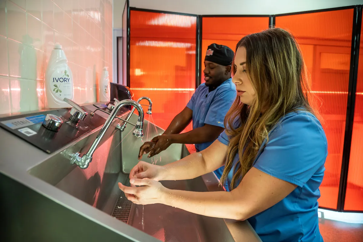 A group of students in scrubs washes their hands before entering the simulation lab on campus.