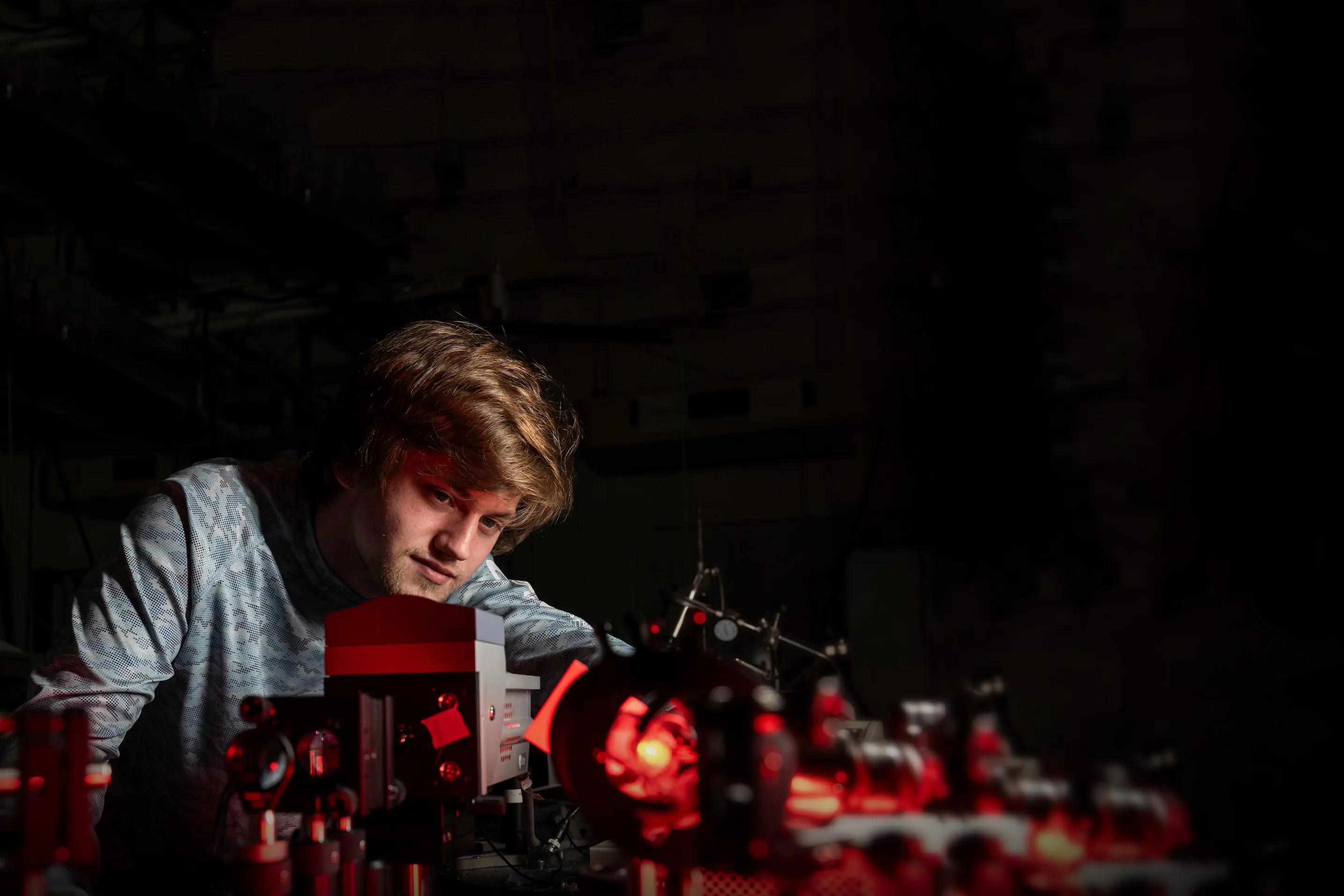 Student conducting physics experiment with laser optics in research lab.