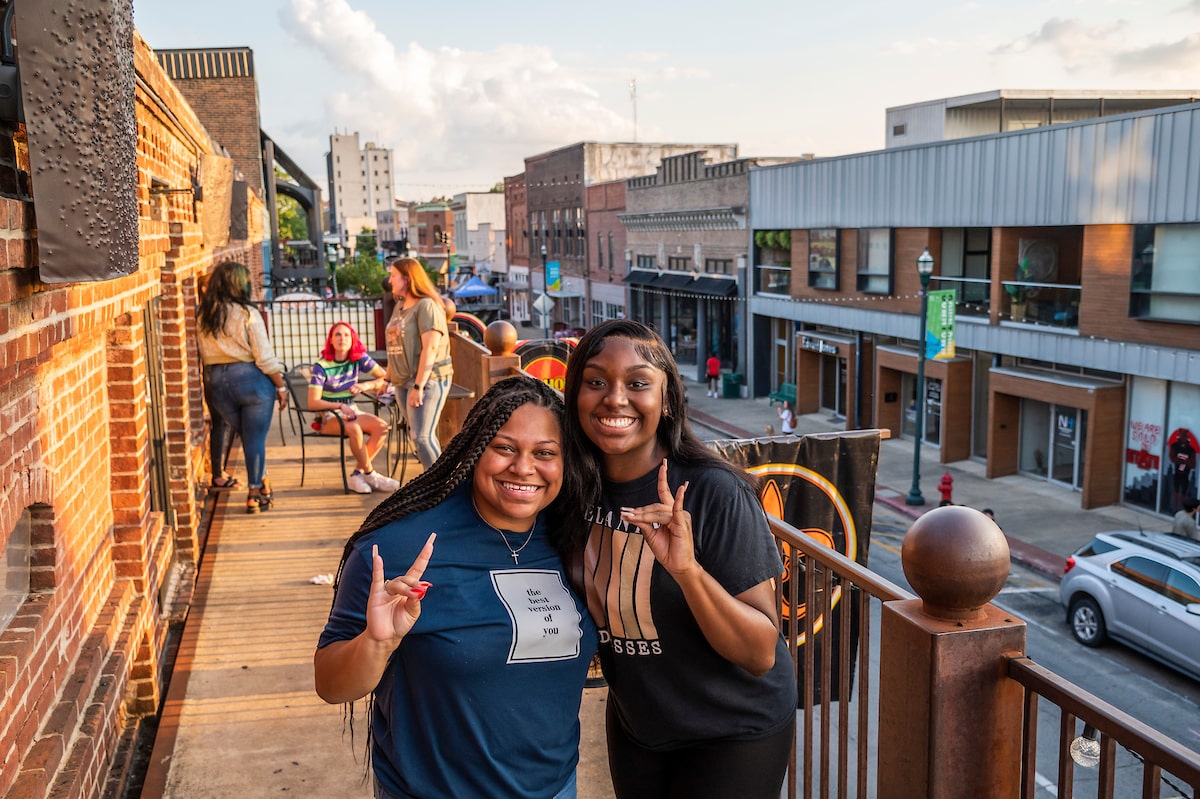 Two women smile on a balcony during a Student Advisory Board block party while overlooking downtown Jonesboro.