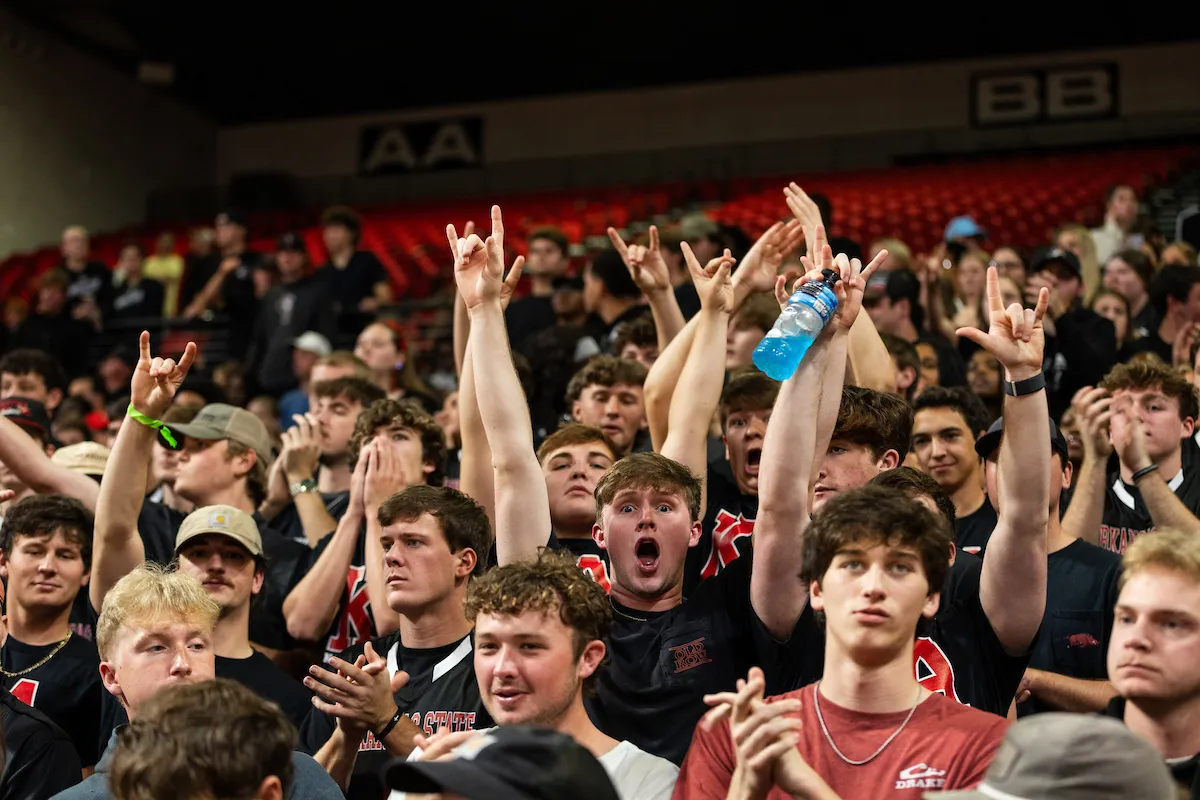 Excited students in black shirts cheer and raise their hands during a home basketball game in the arena.