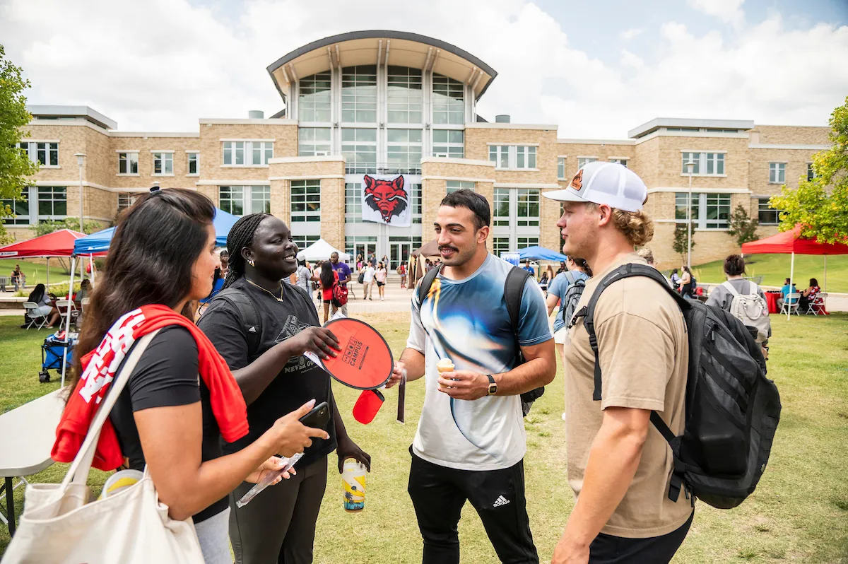 Group of A-State students standing and talking in front of Reng Student Union at annual Community Fair event.