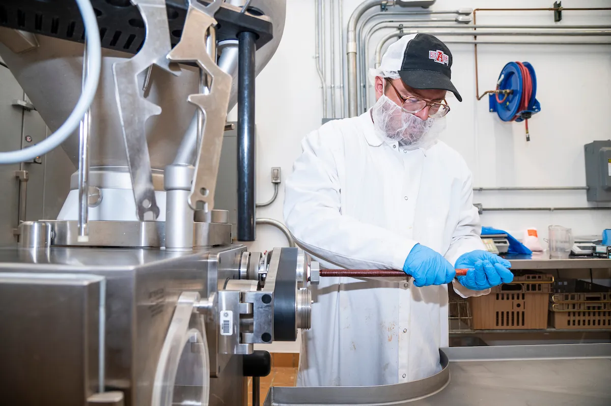 Lab worker in protective gear operates meat processing equipment in a food science lab.