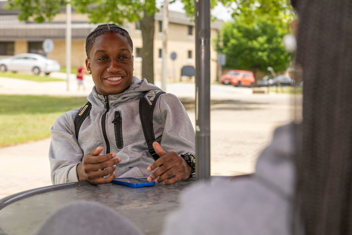 A student smiling and sitting at a table outside.